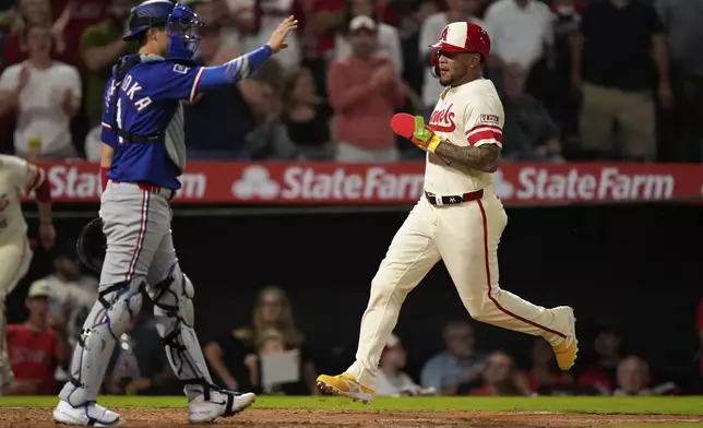 Los Angeles Angels' Yoan Moncada, right, scores on a double by Zach Neto as Texas Rangers catcher Kyle Higashioka gestures during the sixth inning of a baseball game Tuesday, July 29, 2025, in Anaheim, Calif. (AP Photo/Mark J. Terrill)