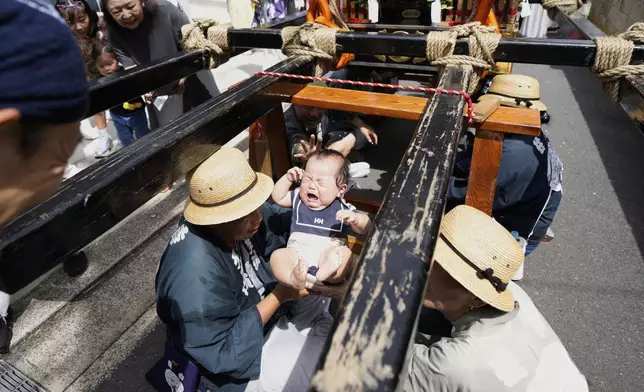 Participants pass a newborn baby underneath a portable shrine, or mikoshi, intended to bring good fortune, during the annual Kurihama Sumiyoshi Shrine Festival at Kurihama, Yokosuka city, south of Tokyo Sunday, July 27, 2025. (AP Photo/Eugene Hoshiko)