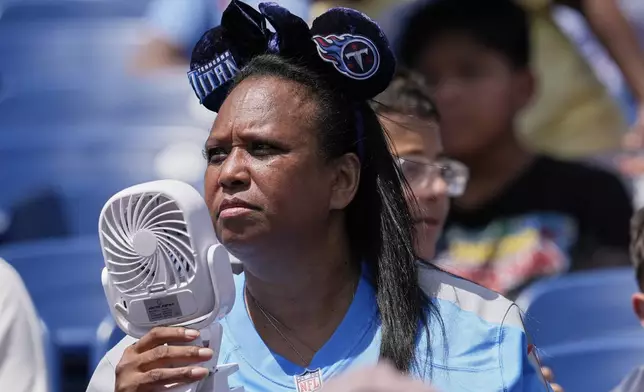 A Tennessee Titans fan uses a fan to keep cool while watching practice during "Back Together Weekend" at the team's NFL football training camp Saturday, July 26, 2025, in Nashville, Tenn. (AP Photo/George Walker IV)