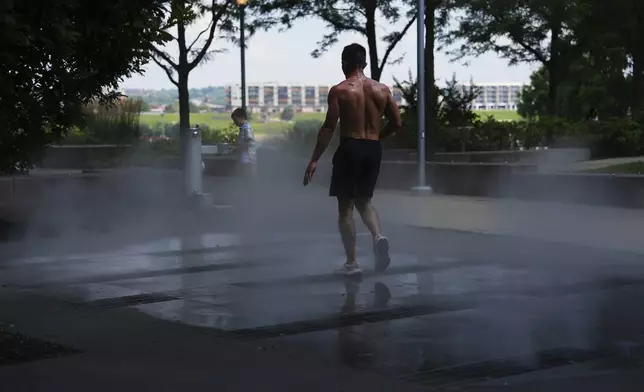 A person walks through a machine that mists to cool off after taking a break from running on a hot day, Friday, July 25, 2025, in Cincinnati. (AP Photo/Joshua A. Bickel)