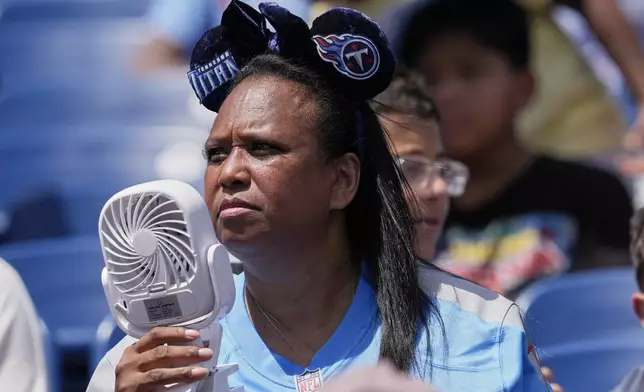 A Tennessee Titans fan uses a fan to keep cool while watching practice during "Back Together Weekend" at the team's NFL football training camp Saturday, July 26, 2025, in Nashville, Tenn. (AP Photo/George Walker IV)