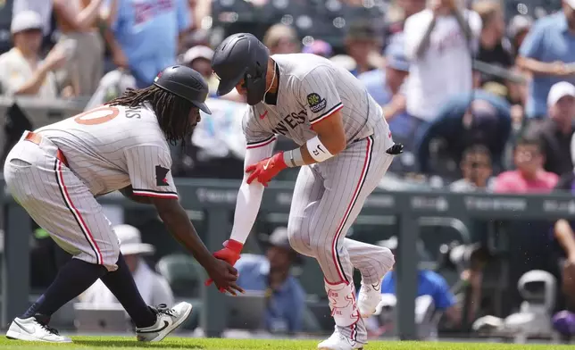 Minnesota Twins third base coach Tommy Watkins, left, congratulates Royce Lewis, right, who circles the bases after hitting a solo home run off Colorado Rockies relief pitcher Ryan Rolison in the fourth inning of a baseball game Sunday, July 20, 2025, in Denver. (AP Photo/David Zalubowski)