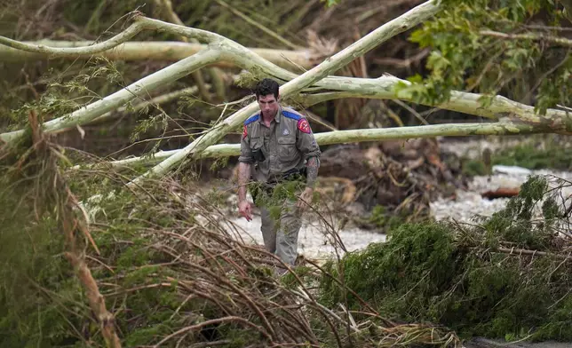 A Texas Department of Public Safety official combs through the banks of the Guadalupe River near Camp Mystic after a flash flood swept through the area Saturday, July 5, 2025, in Hunt, Texas. (AP Photo/Julio Cortez)