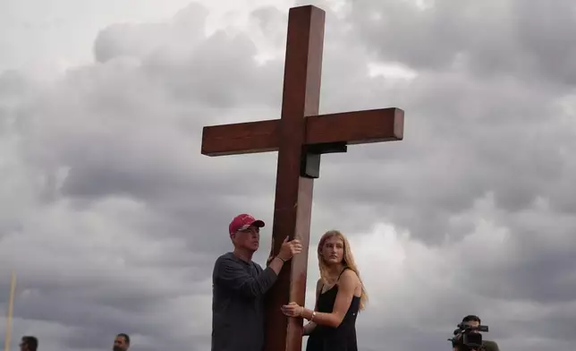Dan Beazley, of Michigan, center left, and Abigail Smithson hold a large cross during a vigil for flooding victims at Tivy Antler Stadium on Wednesday, July 9, 2025, in Kerrville, Texas. (AP Photo/Gerald Herbert)