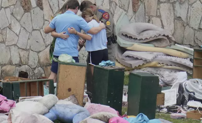An officer prays with a family as they pick up items at Camp Mystic in Hunt, Texas on Wednesday, July 9, 2025. (AP Photo/Ashley Landis)