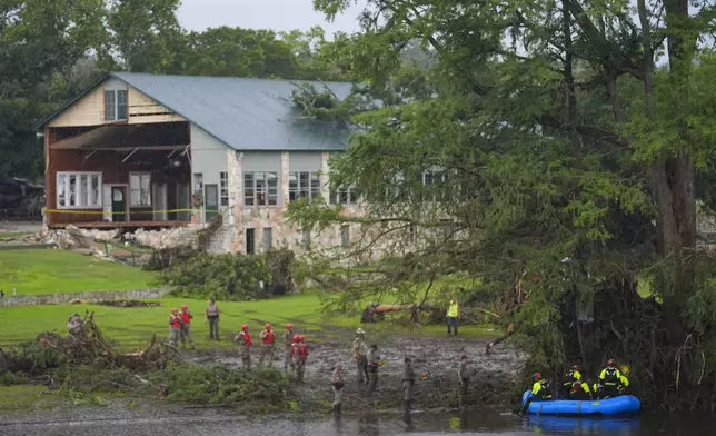Rescue workers are seen on land and on a boat as they search for missing people near Camp Mystic along the Guadalupe River after a flash flood swept through the area Sunday, July 6, 2025, in Hunt, Texas. (AP Photo/Julio Cortez)