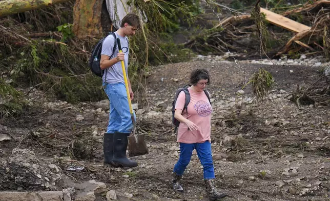 People walk along debris near the banks of the Guadalupe River after a flash flood swept through the area Saturday, July 5, 2025, in Hunt, Texas. (AP Photo/Julio Cortez)