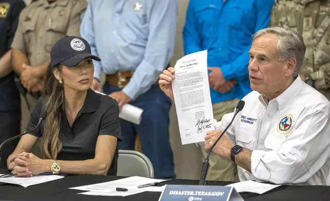 Texas Gov. Greg Abbott signs and holds up an disaster declaration proclamation as Homeland Security Secretary Kristi Noem, left, looks on during a press conference about recent flooding along the Guadalupe River, Saturday, July 5, 2025, in Kerrville, Texas. (AP Photo/Rodolfo Gonzalez)