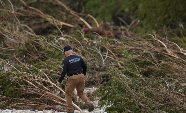 A Sheriff's deputy combs through the banks of the Guadalupe River near Camp Mystic after a flash flood swept through the area Saturday, July 5, 2025, in Hunt, Texas. (AP Photo/Julio Cortez)