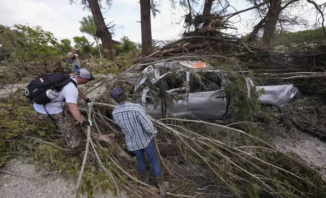Kevin Scott, Danny LeBourgeois and Lincoln Edwards search for Aiden Heartfield, who went camping with friends and is missing, around a damaged truck and branches along the Guadalupe River after flooding in Kerrville, Texas on Wednesday , July 9, 2025. (AP Photo/Gerald Herbert)