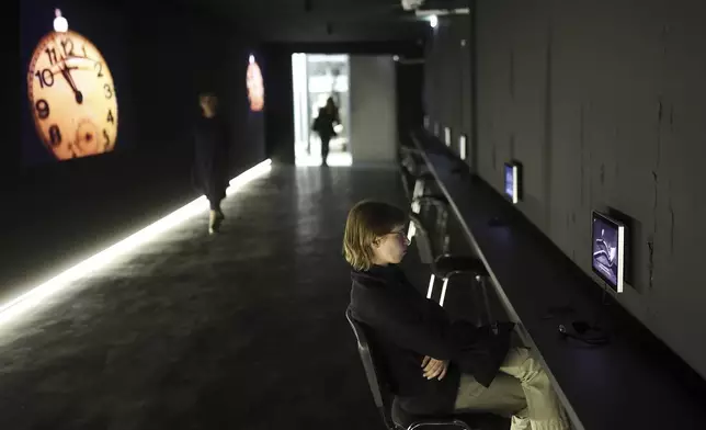 Woman watches a video, part of the exhibition "Lives Beyond the Fields of Death" opened at the Srebrenica Memorial Center in Potocari, Bosnia, Thursday, July 10, 2025. (AP Photo/Armin Durgut)