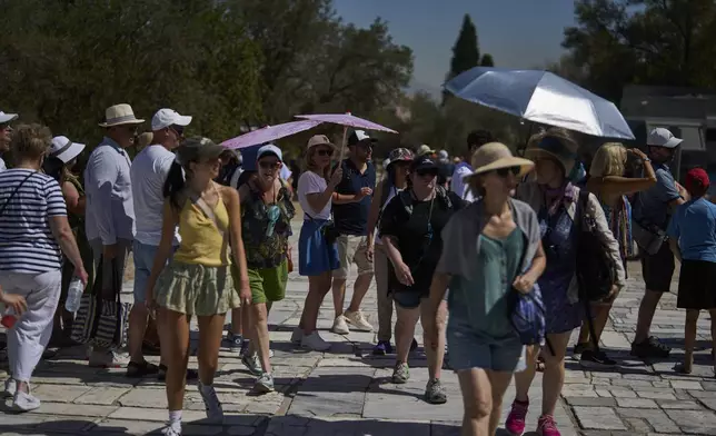 Tourist with umbrellas wait outside the Acropolis of Athens, on Monday , July 7, 2025 while authorities in Greece have imposed mandatory work stoppages in parts of the country where temperatures are expected to exceed 40 degrees Celsius (104 Fahrenheit) (AP Photo/Petros Giannakouris)