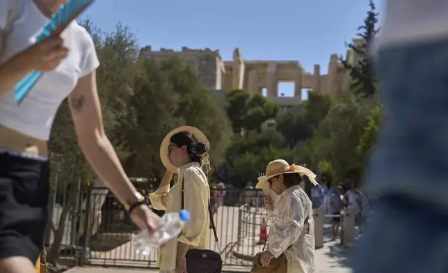 Tourist walk outside the Acropolis of Athens, on Monday, July 7, 2025 while authorities in Greece have imposed mandatory work stoppages in parts of the country where temperatures are expected to exceed 40 degrees Celsius (104 Fahrenheit) (AP Photo/Petros Giannakouris)