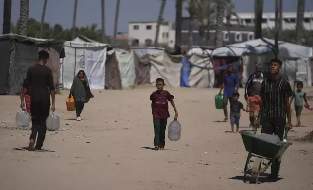 Palestinians carry containers for water at a camp for the displaced in Deir al-Balah, Gaza Strip, Monday, July 7, 2025. (AP Photo/Abdel Kareem Hana)