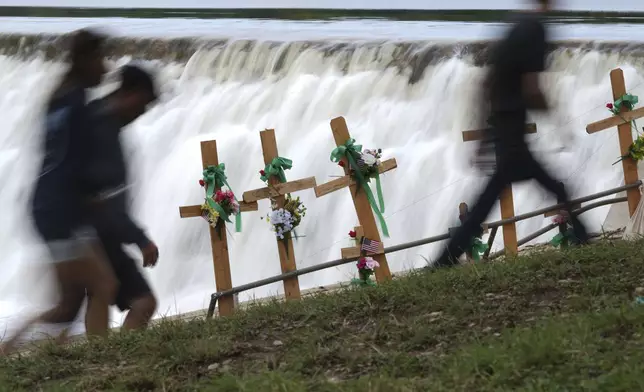 Visitors walk past crosses at a make-shift memorial honoring flood victims, Sunday, July 13, 2025, in Kerrville, Texas. (AP Photo/Eric Gay)