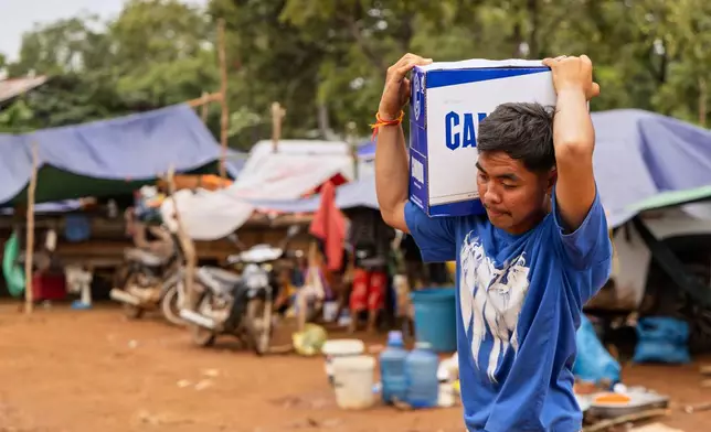 A man carries a box of water handed out at the Battkhao Resettlement Camp for displaced Cambodians in Oddar Meanchey Province on Saturday, July 26, 2025. (AP Photo/Anton L. Delgado)