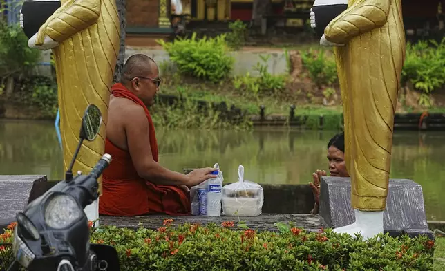 A Cambodian Buddhist monk, left, receives food from a devotee, right, in Wat Prasat Samrong Pagoda in Oddar Meanchey province, Cambodia, Saturday, July 26, 2025, as border fighting between Thailand and Cambodia entered its third day. (AP Photo/Heng Sinith)