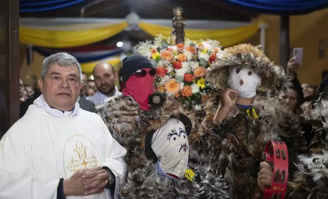 Priest Modesto Martinez joins in a procession after leading a Mass celebrating Saint Francisco Solano, in Emboscada, Paraguay, Thursday, July 24, 2025. Hundreds of Catholic parishioners in Paraguay don bird-like costumes and parade down the streets to honor the 16th century saint said to possess miraculous powers. (AP Photo/Jorge Saenz)