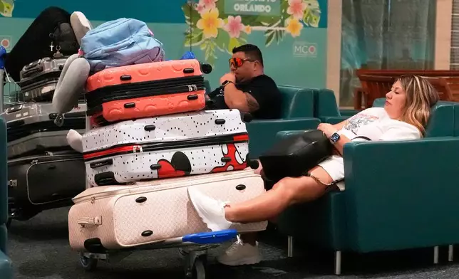 Holiday travelers take a break in the terminal at Orlando International Airport, Thursday, July 3, 2025, in Orlando, Fla. (AP Photo/John Raoux)