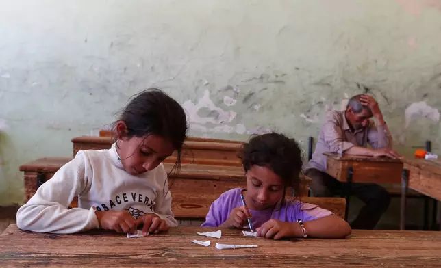 Displaced Bedouin girls who fled with their families from the town of Shahba in southern Sweida province due to clashes between Bedouin clans and Druze militias, draw on scraps of paper inside a classroom turned shelter in the town of Nahtah, in the eastern part of Daraa province, Syria, Monday, July 21, 2025. (AP Photo/Omar Sanadiki)