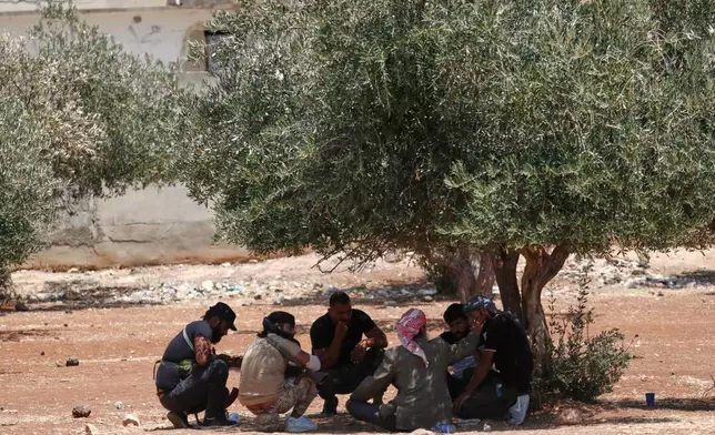 Bedouin fighters sit under the shade of an olive tree outside a temporary shelter housing Bedouin families who fled their homes in Shahba, a town in Syria's southern Sweida province, due to clashes between Bedouin clans and Druze militias, in the town of Nahtah, in the eastern part of Daraa province, Syria, Monday, July 21, 2025. (AP Photo/Omar Sanadiki)