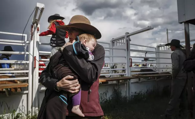 Courtney Beverly, from Winfield, Alberta, holds her nine month old daughter Rowelly-Dee Phillips as the rest of her family gather to support her in women's ranch bronc during rodeo action in Crossfield, Alberta, Saturday, June 14, 2025. (Jeff McIntosh/The Canadian Press via AP)