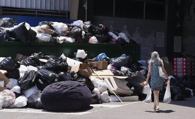 A woman drops off trash at a garbage collection site, Thursday, July 3, 2025, in Philadelphia. (AP Photo/Matt Slocum)