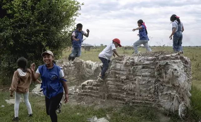 Young Indigenous guards play on the walls of an old military defense barrier made of sandbags, remnants of the military occupation in the area, on July, 19, 2025, in the Lopez Adentro reserve in Caloto, Colombia. (AP Photo/Nadège Mazars)