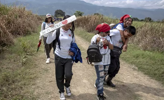 Indigenous youth, part of the children's semillero, a school that prepares the next generation to protect their ancestral land, bring a sign to hang that reads: "Be the change" on July, 19, 2025, in the Lopez Adentro reserve in Caloto, Colombia. (AP Photo/Nadège Mazars)