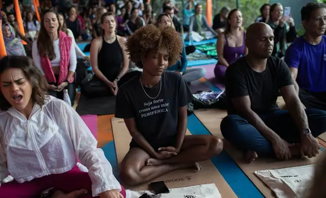 A woman sitting in the lotus position wears a shirt that reads in Portuguese, "Be strong like a mother from the outskirts" while meditating during a Transformation Project yoga class in the Rocinha favela, in Rio de Janeiro, Wednesday, July 9, 2025. (AP Photo/Bruna Prado)
