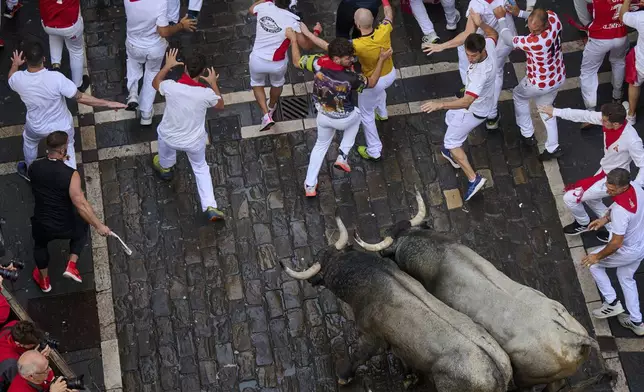Revelers run alongside José Escolar Gil's fighting bulls during the sixth running of the bulls at the San Fermín Festival in Pamplona, Spain, Saturday, July 12, 2025. (AP Photo/Miguel Oses)