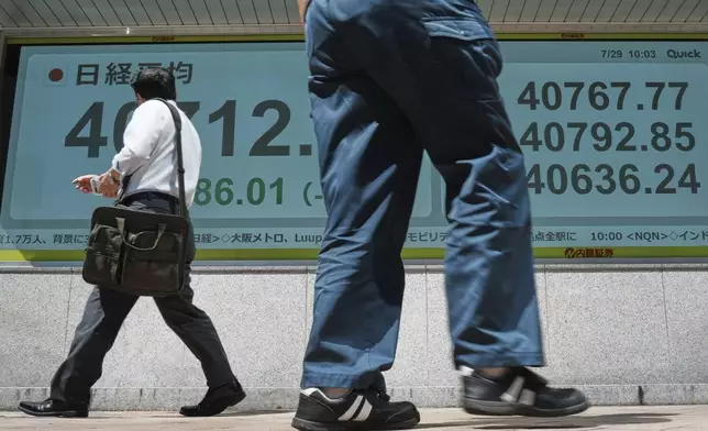 Persons walk in front of an electronic stock board showing Japan's Nikkei index at a securities firm Tuesday, July 29, 2025, in Tokyo. (AP Photo/Eugene Hoshiko)