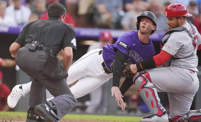 As home plate umpire Willie Trynor, left, waits to make the call as Colorado Rockies' Ryan McMahon, center, is tagged out by St. Louis Cardinals catcher Pedro Pagés, right, while trying to score on a ground ball hit by Rockies' Yanquiel Fernández in the second inning of a baseball game Monday, July 21, 2025, in Denver. (AP Photo/David Zalubowski)