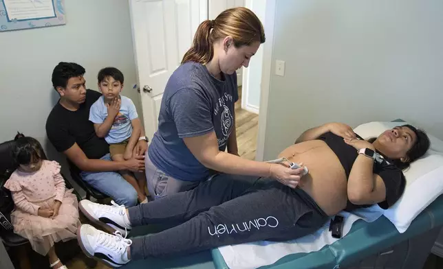 Simone Payan, a nurse-midwife at Holy Family Services, a birth center and women's clinic in the Rio Grande Valley, examines Veronica Mendez, 28, who is due with her third child in August, next to Mendez's husband, Erik Pelagio, 29, and their children, Eleanor Pelagio, 3, and Romeo Pelagio, 5, during her appointment at the center in the Rio Grande Valley, Tuesday, June 17, 2025, in Weslaco, Texas. The family, who are from Mexico, have a business visa that doesn't allow them to enroll in federally-funded health insurance programs like Medicaid. (AP Photo/Jacquelyn Martin)