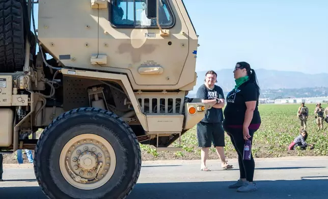 Rebecca Torres stands in front of a military vehicle approaching a federal immigration agents raid in the agriculture area of Camarillo, Calif., Thursday, July 10, 2025. (AP Photo/Michael Owen Baker)