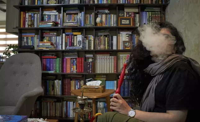 In a city emptied by war, a woman smokes hookah with a friend at home in Tehran, Iran, Tuesday, June 17, 2025. (AP Photo)