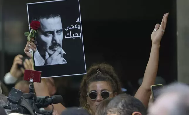 A mourner holds up a portrait of Ziad Rahbani, a visionary Lebanese composer, playwright, pianist and political provocateur, who died last Saturday at age 69, as she marches during Rahbani's funeral in Beirut, Lebanon, Monday, July 28, 2025. (AP Photo/Hussein Malla)