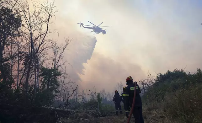 Firefighters try to extinguish the blazes in a forest as a helicopter drops water during a wildfire, in the northwestern suburb of Kryoneri, in Athens, Greece, Saturday, July 26, 2025. (AP Photo/Yorgos Karahalis)