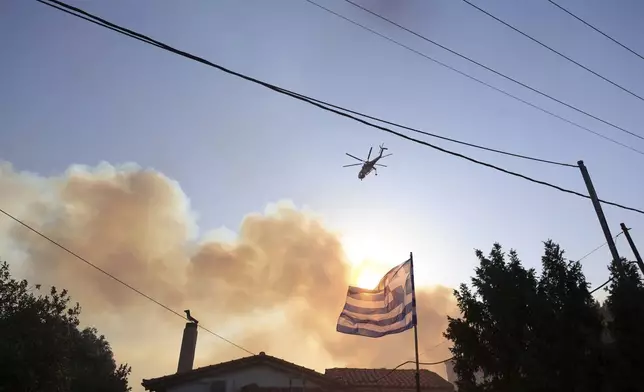 A helicopter flies over a burning area during a wildfire, in the northwestern suburb of Kryoneri, in Athens, Greece, Saturday, July 26, 2025. (AP Photo/Yorgos Karahalis)
