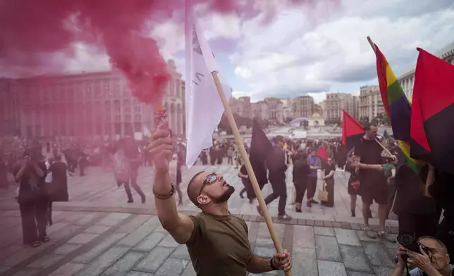 A man holds color smoke during the farewell ceremony of David Chichkan, a Ukrainian serviceman and artist at Independence square in Kyiv, Ukraine, on Monday, Aug. 18, 2025. (AP Photo/Evgeniy Maloletka)