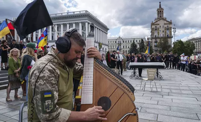 A Ukrainian soldier plays on Bandura during the farewell ceremony of David Chichkan, a Ukrainian serviceman and artist at Independence square in Kyiv, Ukraine, on Monday, Aug. 18, 2025. (AP Photo/Evgeniy Maloletka)