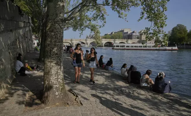 People sit in the shade along the Seine river during a sunny day in Paris, Sunday, Aug. 10, 2025. (AP Photo/Michel Euler)