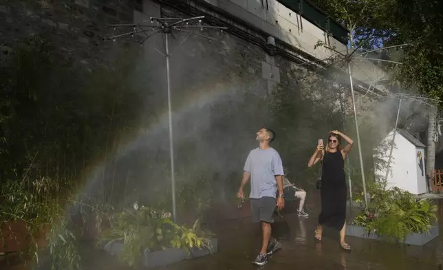 People cool off under showers at Paris Plage along the Seine river in Paris, Sunday, Aug. 10, 2025. (AP Photo/Michel Euler)