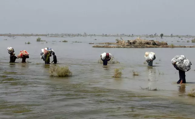FILE - Victims of heavy flooding from monsoon rains carry relief aid through floodwater in the Qambar Shahdadkot district of Sindh Province, Pakistan, Sept. 9, 2022. (AP Photo/Fareed Khan, File)