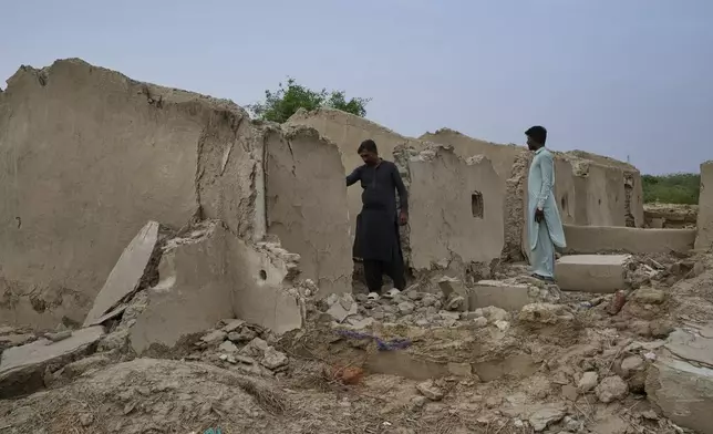 Villagers look at houses damaged by climate-induced floods several years ago at a village in Umerkot, a district of Pakistan's southeastern Sindh province, Thursday, July 17, 2025. (AP Photo/Fareed Khan)