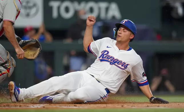 Texas Rangers' Corey Seager slides into home while scoring on a single by teammate Marcus Semien during the first inning of a baseball game against the Philadelphia Phillies Saturday, Aug. 9, 2025, in Arlington, Texas. (AP Photo/Julio Cortez)