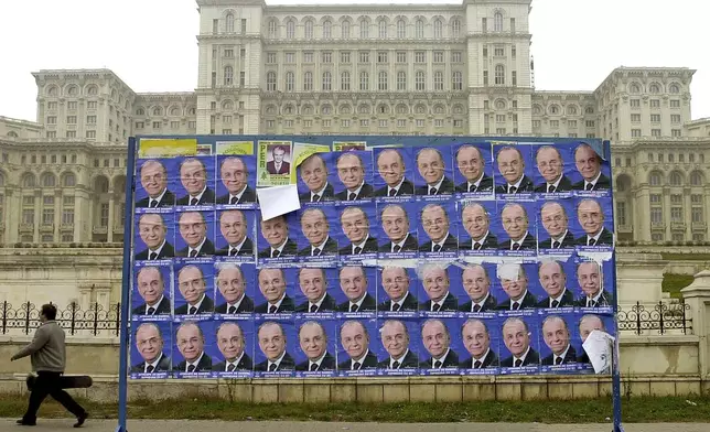 FILE - A man passes by posters of former Romanian President Ion Iliescu, backdropped by the communist-era House of the People, currently the Palace of Parliament in Bucharest Saturday Nov. 25, 2000.(AP Photo/Vadim Ghirda, File)
