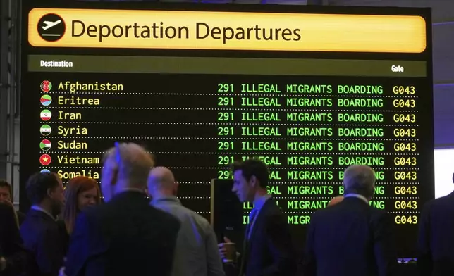 Journalists and party members are seen in front of a mock departures board before British Reform party leader Nigel Farage addresses journalists during a press conference in a hangar at Oxford Airport in Kidlington, England, Tuesday, Aug. 26, 2025. (AP Photo/Joanna Chan)