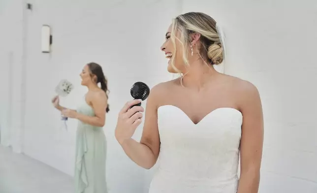Kayla McDonald, right, uses a small electric fan to keep cool while taking bridal portraits with her sister, Jessica McDonald, left, before her wedding Saturday, Aug. 23, 2025, in Newtown, Ohio. (AP Photo/Joshua A. Bickel)