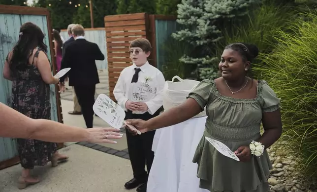 Zuri Jones, right, hands a fan to a guest as they arrive for a wedding Saturday, Aug. 23, 2025, in Newtown, Ohio. (AP Photo/Joshua A. Bickel)